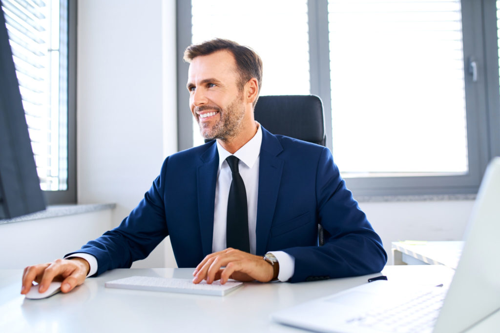 Smiling businessman sitting in front of office computer and working